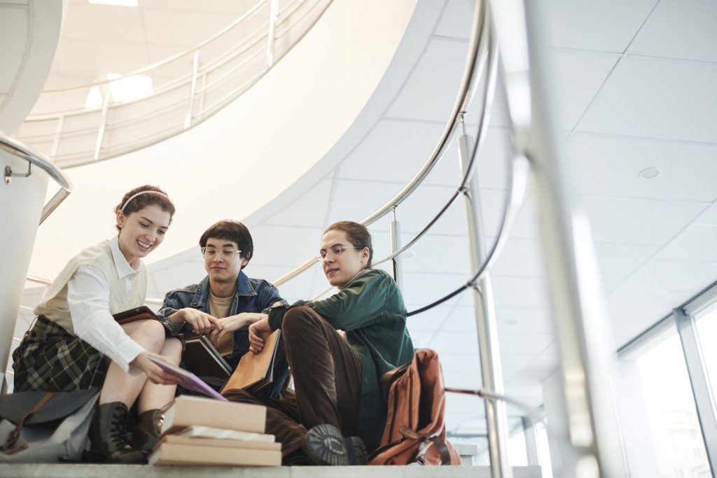 Three diverse students collaborating and studying on an indoor stairway, fostering teamwork and friendship.