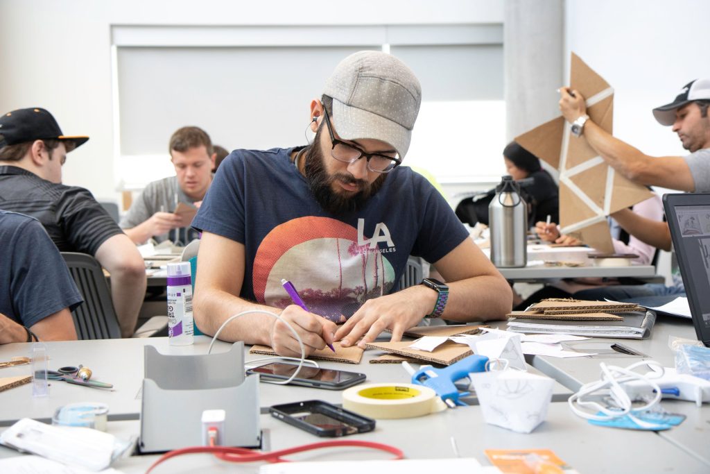 University students working on a cardboard craft project in a classroom.